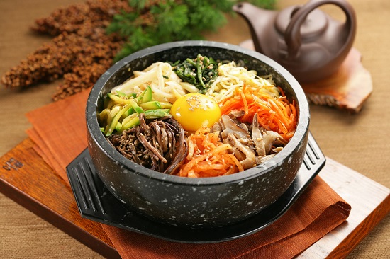 Cách thực hiện cơm trộn Bibimbap Hàn Quốc: Bước 1: Chuẩn bị nước sốt cho cơm trộn Cho tất cả nguyên liệu: 2 tép tỏi, 1/3 trái táo, 1/2 củ hành tây, nước cốt của 1/2 trái chanh, 2 muỗng canh tương ớt Hàn Quốc Gochujang, 1 muỗng canh rượu Mirin, 1 muỗng canh dầu mè, 1/2 muỗng canh nước tương Hàn Quốc, 1/2 muỗng canh đường nâu, 1/2 muỗng canh siro bắp, 1/4 muỗng cà phê tiêu vào máy xay sinh tố, xay mịn. Bước 2: Phần cơm trộn Thịt bò rửa sạch, cắt nhỏ, đem ướp với 1 muỗng canh rượu Mirin ( ta có thể thay thế rượu khác hoặc có thể bỏ qua nếu bạn dị ứng với nó), 1/2 muỗng canh nước tương Hàn Quốc, 1/2 muỗng canh dầu mè, 1/2 muỗng canh đường nâu, 1/4 muỗng cà phê tiêu,  sau đó để 15 phút cho thịt thấm tất cả các gia vị. Bước 3: Sơ chế, xào rau củ Giá đỗ và cải bó xôi rửa sạch, cải bó xôi đem cắt khúc khoảng 10cm. Cải bó xôi có thể sau khi rửa sạch có thể để nguyên cọng, luộc xong hãy cắt nhỏ ra Bắc một nồi nước, cho vào 1 ít muối, khi nước sôi bùng thì cho giá đỗ vào luộc trước, sau 2 phút thì vớt giá ra, cho cải bó xôi vào tiếp tục luộc 2 phút, vớt ra. Để riêng 2 loại rau, mỗi loại trộn với 1/2 muỗng cà phê muối tiêu và 1 muỗng cà phê dầu mè. Bước 4: Chế biến rau củ quả Cà rốt, bí ngòi rửa sạch, cắt sợi khoảng 5cm. Nấm đông cô rửa sạch, cắt bỏ chân, đem cắt lát mỏng. Để lửa lớn, cho vào chảo 1 muỗng canh dầu ăn, thêm bí ngòi vào xào đến khi gần chín thì nêm với 1 muỗng cà phê dầu mè, 1/2 muỗng cà phê muối tiêu, trút bí ngòi ra dĩa. Cho lần lượt 2 loại còn lại vào xào riêng, nếu hết dầu thì châm thêm 1 muỗng canh dầu vào, xào và nêm nếm tương tự như bí ngòi. Bước 5: Nấu cơm Thường là dùng gạo của Hàn Quốc để nấu cho đúng vị. Nhưng ta có thể thay thế bằng gạo Việt cho hợp khẩu vị. Ta nấu trong thố nhỏ để giữ được độ nấu hoặc ta có thể nấu trong nồi cơm điện, sau đó múc vào thố để ăn Cho vào thố 1 muỗng cà phê dầu mè, dùng cọ phết cho dầu đều đáy thố. Múc cơm vào và dàn đều cơm. Xếp lần lượt các loại rau củ, thịt bò xào, kim chi cắt nhỏ vào rồi đặt thố lên bếp, bật lửa đun đến khi lớp cơm ở dưới nóng giòn, nghe tiếng xèo xèo thì nhắc xuống. Trứng gà cho vào chảo, ốp la trứng vừa đủ chín tới, lòng đào còn chưa chín. Đặt trứng vào thố cơm, rắc ít mè rang lên trên. Bước 6: Thành phẩm Khi ăn bạn cho sốt tương vào, trộn đều. Món cơm trộn nóng hổi đầy đủ dưỡng chất đảm bảo hấp dẫn đến từng muỗng cuối cùng.