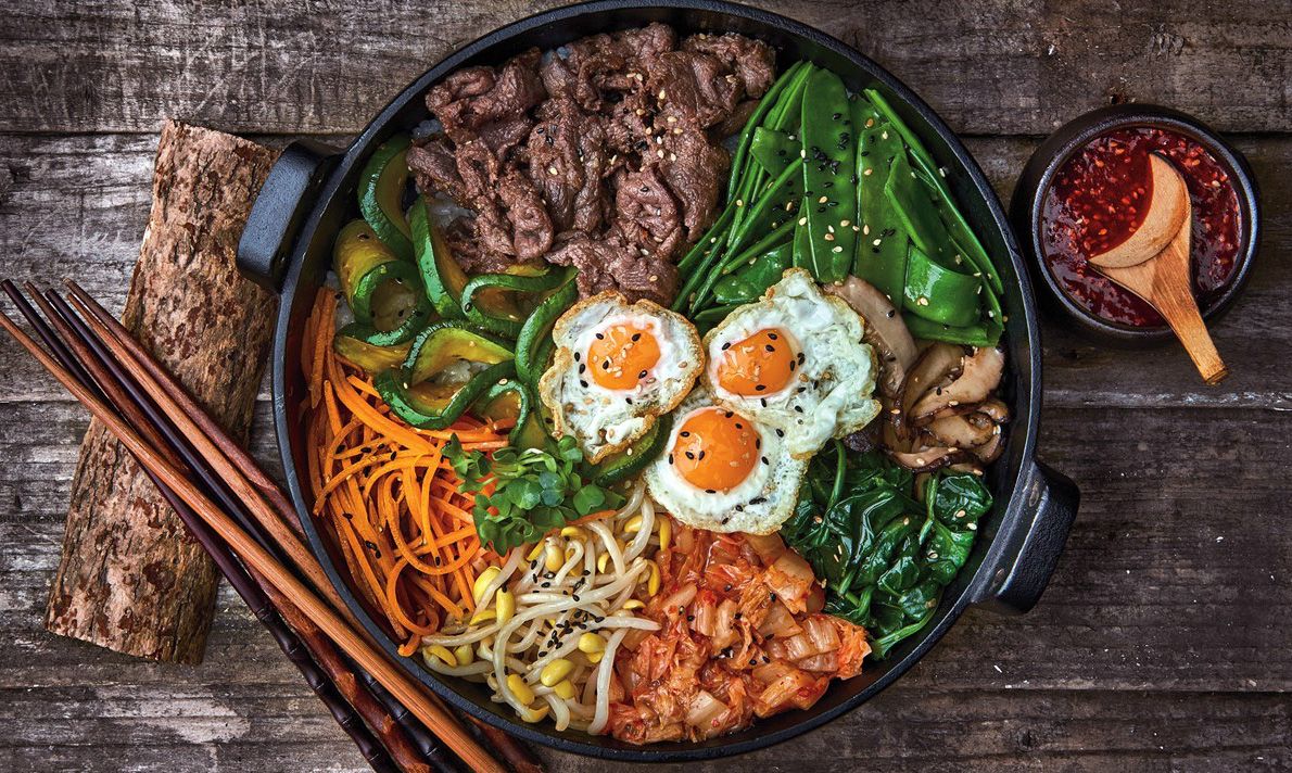 Cách thực hiện cơm trộn Bibimbap Hàn Quốc: Bước 1: Chuẩn bị nước sốt cho cơm trộn Cho tất cả nguyên liệu: 2 tép tỏi, 1/3 trái táo, 1/2 củ hành tây, nước cốt của 1/2 trái chanh, 2 muỗng canh tương ớt Hàn Quốc Gochujang, 1 muỗng canh rượu Mirin, 1 muỗng canh dầu mè, 1/2 muỗng canh nước tương Hàn Quốc, 1/2 muỗng canh đường nâu, 1/2 muỗng canh siro bắp, 1/4 muỗng cà phê tiêu vào máy xay sinh tố, xay mịn. Bước 2: Phần cơm trộn Thịt bò rửa sạch, cắt nhỏ, đem ướp với 1 muỗng canh rượu Mirin ( ta có thể thay thế rượu khác hoặc có thể bỏ qua nếu bạn dị ứng với nó), 1/2 muỗng canh nước tương Hàn Quốc, 1/2 muỗng canh dầu mè, 1/2 muỗng canh đường nâu, 1/4 muỗng cà phê tiêu,  sau đó để 15 phút cho thịt thấm tất cả các gia vị. Bước 3: Sơ chế, xào rau củ Giá đỗ và cải bó xôi rửa sạch, cải bó xôi đem cắt khúc khoảng 10cm. Cải bó xôi có thể sau khi rửa sạch có thể để nguyên cọng, luộc xong hãy cắt nhỏ ra Bắc một nồi nước, cho vào 1 ít muối, khi nước sôi bùng thì cho giá đỗ vào luộc trước, sau 2 phút thì vớt giá ra, cho cải bó xôi vào tiếp tục luộc 2 phút, vớt ra. Để riêng 2 loại rau, mỗi loại trộn với 1/2 muỗng cà phê muối tiêu và 1 muỗng cà phê dầu mè. Bước 4: Chế biến rau củ quả Cà rốt, bí ngòi rửa sạch, cắt sợi khoảng 5cm. Nấm đông cô rửa sạch, cắt bỏ chân, đem cắt lát mỏng. Để lửa lớn, cho vào chảo 1 muỗng canh dầu ăn, thêm bí ngòi vào xào đến khi gần chín thì nêm với 1 muỗng cà phê dầu mè, 1/2 muỗng cà phê muối tiêu, trút bí ngòi ra dĩa. Cho lần lượt 2 loại còn lại vào xào riêng, nếu hết dầu thì châm thêm 1 muỗng canh dầu vào, xào và nêm nếm tương tự như bí ngòi. Bước 5: Nấu cơm Thường là dùng gạo của Hàn Quốc để nấu cho đúng vị. Nhưng ta có thể thay thế bằng gạo Việt cho hợp khẩu vị. Ta nấu trong thố nhỏ để giữ được độ nấu hoặc ta có thể nấu trong nồi cơm điện, sau đó múc vào thố để ăn Cho vào thố 1 muỗng cà phê dầu mè, dùng cọ phết cho dầu đều đáy thố. Múc cơm vào và dàn đều cơm. Xếp lần lượt các loại rau củ, thịt bò xào, kim chi cắt nhỏ vào rồi đặt thố lên bếp, bật lửa đun đến khi lớp cơm ở dưới nóng giòn, nghe tiếng xèo xèo thì nhắc xuống. Trứng gà cho vào chảo, ốp la trứng vừa đủ chín tới, lòng đào còn chưa chín. Đặt trứng vào thố cơm, rắc ít mè rang lên trên. Bước 6: Thành phẩm Khi ăn bạn cho sốt tương vào, trộn đều. Món cơm trộn nóng hổi đầy đủ dưỡng chất đảm bảo hấp dẫn đến từng muỗng cuối cùng.