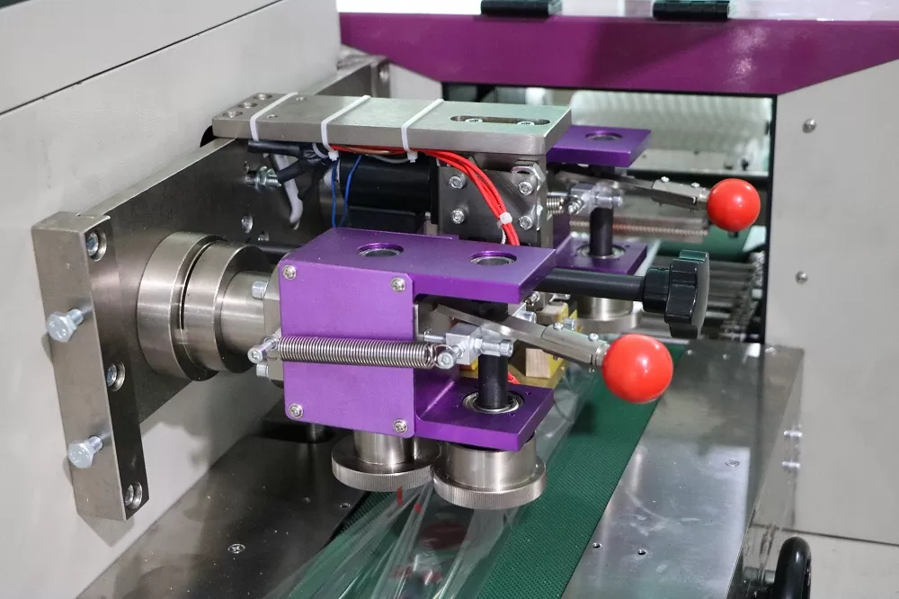 Cách thức hoạt động của thiết bị: Băng tải hoạt động: Là chìa khóa cơ khí trong bộ phận của thiết được làm bằng thép không gỉ, phù hợp với thực phẩm QS. Bảng tải truyền mọi hoạt động từ khâu đóng gói xúc xích đến với nhân công để sắp xếp phù hợp bỏ vào thùng Thiết bị làm phồng túi: Tự động cuộn phim hình thành hình dạng túi, linh hoạt trong sản xuất với các dạng kích thước khác nhau và thuận tiện cho cơ sở là không cần điều chỉnh quá nhiều lần cho các sản phẩm khác nhau nên tiết kiệm được thời gian Màn hình cảm ứng: Được cài đặt với nhiều ngôn ngữ khác nhau nên có thể điều chỉnh sao cho phù hợp môi trường làm việc của bạn. Màn hình cảm ứng với kích thước lớn nên dễ dàng cài đặt, hiện thị rõ các thông số và có thể dừng mọi hoạt động chỉ với một nút bấm Dao cắt và niêm phong sản phẩm: Bộ phận dao hoạt động liên tục để cắt sản phẩm sao cho đúng vị trí Định hình vị trí: Sử dụng bên ngoài phim vị trí cấu trúc, bao bì phim cài đặt là đơn giản hơn và một cách nhanh chóng hơn cho việc sản xuất
