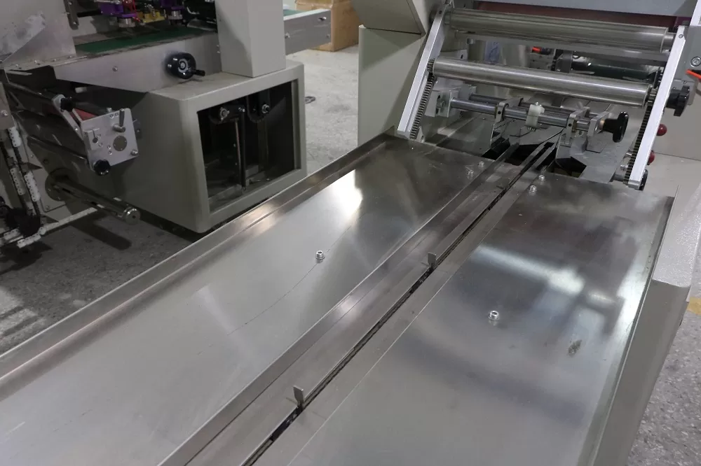 Cách thức hoạt động của thiết bị: Băng tải hoạt động: Là chìa khóa cơ khí trong bộ phận của thiết được làm bằng thép không gỉ, phù hợp với thực phẩm QS. Bảng tải truyền mọi hoạt động từ khâu đóng gói xúc xích đến với nhân công để sắp xếp phù hợp bỏ vào thùng Thiết bị làm phồng túi: Tự động cuộn phim hình thành hình dạng túi, linh hoạt trong sản xuất với các dạng kích thước khác nhau và thuận tiện cho cơ sở là không cần điều chỉnh quá nhiều lần cho các sản phẩm khác nhau nên tiết kiệm được thời gian Màn hình cảm ứng: Được cài đặt với nhiều ngôn ngữ khác nhau nên có thể điều chỉnh sao cho phù hợp môi trường làm việc của bạn. Màn hình cảm ứng với kích thước lớn nên dễ dàng cài đặt, hiện thị rõ các thông số và có thể dừng mọi hoạt động chỉ với một nút bấm Dao cắt và niêm phong sản phẩm: Bộ phận dao hoạt động liên tục để cắt sản phẩm sao cho đúng vị trí Định hình vị trí: Sử dụng bên ngoài phim vị trí cấu trúc, bao bì phim cài đặt là đơn giản hơn và một cách nhanh chóng hơn cho việc sản xuất